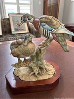 Front and side views of the Kaiser porcelain wood duck sculpture showing detailed painting and realistic posing of the two ducks on a branch with wooden base.