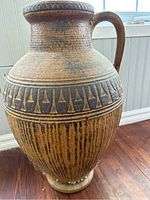 Full view of large pottery jug/vase with handle and geometric patterns under window light.