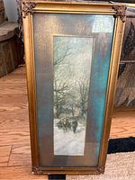 Vertical framed print showing detailed winter scene with man and horse in snow, gold-toned decorative frame with damage and spotting on mat.