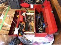 Red metal toolbox with open compartments filled with various hand tools placed on a wooden surface.