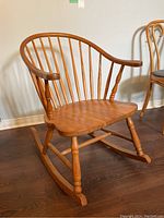 Front-angle view of the wooden Windsor style rocking chair showing curved back with multiple slender vertical spindles and turned arm supports.
