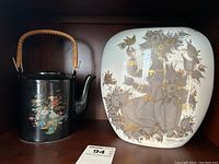 Photo showing the black teapot with bamboo handle next to the square Rosenthal vase with Asian themed artwork.
