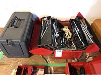 Photo of the black plastic toolbox closed and the red metal cantilever toolbox open showing various hand tools inside.