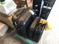 Two black hard shell suitcases side by side, smaller carry-on on the right with a yellow fabric tied to the handle, larger checked bag on the left.