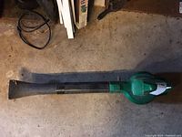 Side view of electric blower showing green cylindrical body and extended black nozzle.