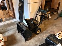 Side view of full snow blower unit showing engine, handle bars, and auger housing.