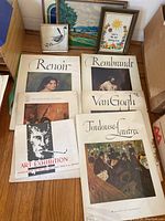 Photo showing five large art folders laid out on the floor, each labeled with a famous artist's name (Renoir, Rembrandt, Van Gogh, Toulouse-Lautrec) plus an art exhibition folder. Print images partially visible through clear plastic covers or on covers.