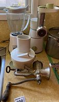 Oster blender with glass pitcher and white base, electric meat grinder, AlexanderWerks manual hand meat grinder all on kitchen counter.