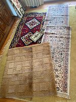 Six area rugs stacked or laid out on each other showing variety in colors and patterns, with one prominent tan shag rug covering parts of other rugs to highlight its texture and backing.