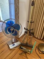 Vintage Crystal Zephyr fan with blue blades, picture light, and TV tray holder on hardwood floor near window and curtains.