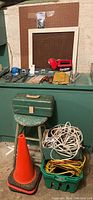 Full lot overview displaying stool, toolbox, orange traffic cone, rolls of cable, green crate with cords, pegboard and work tools on table