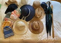 All hats, umbrellas and shoe horn arranged on white quilted bedspread showing variety and quantity.