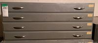 Front view of gray metal four drawer map storage cabinet with silver handles and small yellow labels.
