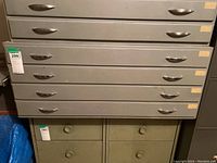 Front view of the grey map storage cabinet with four drawers and silver metal handles. Unit has some minor wear marks and small white labels on the right of each drawer.