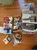 Wide shot of the lot showing three boxes and a bag with various items: a large box filled with maps, a smaller box with matchbooks, a bag of colorful magnets, and a box of shower caps visible under others.