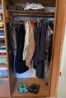 Men’s jackets, shirts, and pants hanging on a clothes rack with two pairs of sandals on the floor
