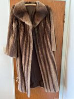 Front view of long brown striped mink fur coat with wide collar hanging on a door.