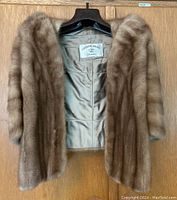 Front view of brown mink fur stole on wooden hanger showing lining and exterior fur.