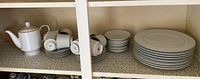 Wide shelf view showing stacked plates, teacups, saucers, and teapot.