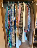 Clothes hanging on a rack showing a variety of jackets, coats, dresses and skirts in floral and patterned fabrics with neutral and muted tones.