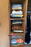 Shelves with folded sweaters and pants hanging on the right side inside a wooden closet