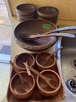 Photo showing the large wooden salad bowl with pewter inlay border, two wooden serving utensils with pewter handles resting inside the bowl, and six small wooden bowls with small wooden spoons around it.