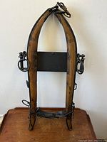 Front view of the horse hames showing wooden frames, cast-iron rings and buckles, leather straps, and metal inscribed sheet.