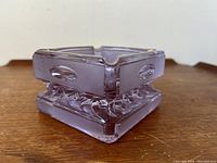 Side angle view showing the light purple color, squarish cubist form, and rounded rectangular indents on the walls of the ashtray.