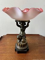 Full view of centerpiece showing cherub figure holding pink ruffled glass bowl above.