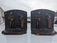 Front view showing both bronze finished cast-iron Angelus bookends side by side with detailed domain scene and inscription at base.