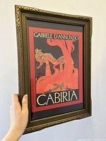Angle view of framed Cabiria Italian movie poster showing ornate wooden gold-tone frame and art deco poster design of nude female figure.