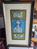 Framed triptych artwork showing three panels with birds and a flute player, under glass in brown frame with white matting.