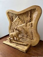 Front angled view of the carved pine wood diorama showing the moose, logs, and mountain forest background.