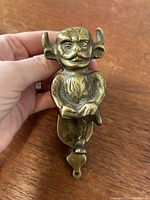 Front view of brass Lincoln Imp door knocker held in hand, showing detailed facial features and seated position.