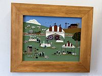 Front view of the folk art painting depicting an Amish county fair scene with tents, people, and animals in a green field, framed in wood.