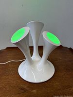 Front view of lamp with greenish light on two trumpet heads and white central trumpet, placed on wooden surface.