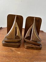 Front view of the pair of wooden sailboat carved bookends placed side by side on a wooden surface.