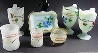 Seven glass souvenir pieces from various Ontario towns, featuring milk and clear glass with floral designs and town names.