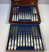 Open two-layer box showing full set of 12 knives and 12 forks with mother-of-pearl handles on blue velvet