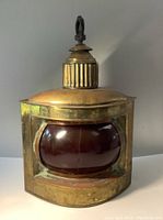 Front view of antique brass ship lantern showing curved red glass globe and brass construction with hook on top.