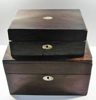 Front view of two stacked antique wooden boxes showing mother of pearl keyhole escutcheons and oval inlays on lids. Larger box on bottom, smaller on top.