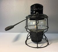 Front view of black metal CPR railway lantern with clear glass globe and wire cage, wooden handle extended, showing overall used condition.