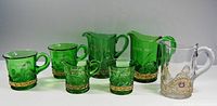 Seven pressed glass souvenir drinking cups and toothpick holder arranged in a row, green with gilt bands and clear piece with decorative gold overlay and red gem.