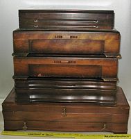 Five stacked vintage wooden cutlery boxes showing the exterior of the largest at bottom and smaller on top
