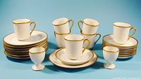 Full set of seven trios of demi-tasse cups with saucers and side plates, plus two egg cups, displayed against blue background.