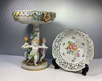Photo showing the pierced floral Schumann Bavarian bowl and German compote with cherubs side by side on display.