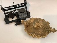 Two metal ink stands, gold-tone with cherubs and black metal with glass ink well, shown side by side.