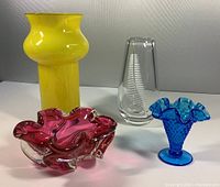 Four mid century modern art glass pieces arranged together: yellow cased vase, clear Orrefors engraved vase, pink ruffled candy dish, blue hobnail Fenton vase