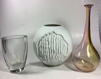 Three modern vases including clear crystal etched nude vase on left, white textured ceramic vase center, and tall blown glass rainbow bud vase right