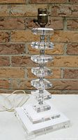 Full view of stacked lucite table lamp showing clear and opaque white lucite squares stacked on pyramid style footed base with brass colored socket at top.
